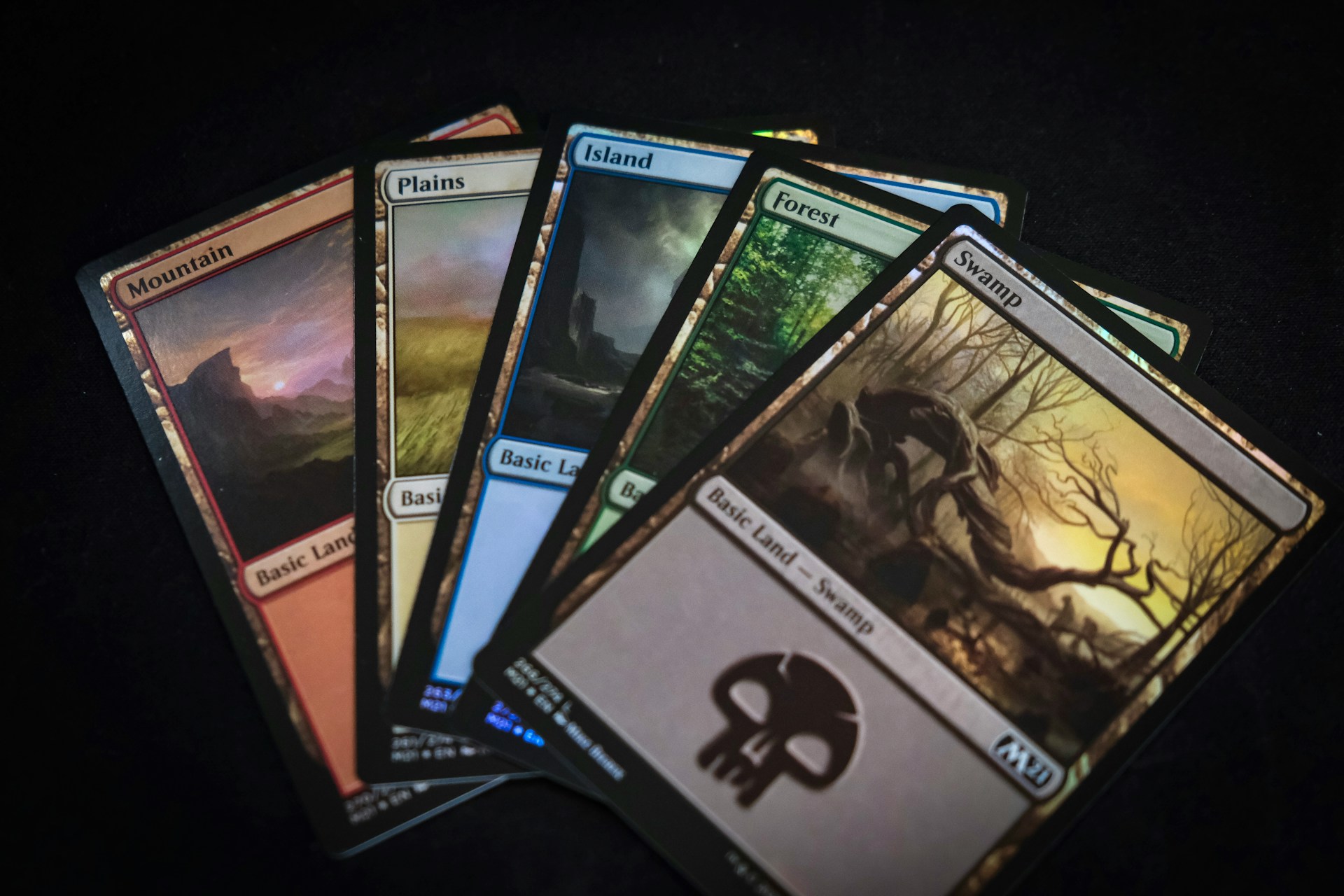 Five Magic: The Gathering basic land cards fanned out on a dark background, the kind of low-value singles that need the best top loaders for shipping trading cards safely on eBay